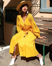 Saffron yellow linen kaftan maxi dress with navy geometric embroidery, balloon sleeves and tassel tie, styled with straw hat, seated lifestyle view - Zalxndra Resort