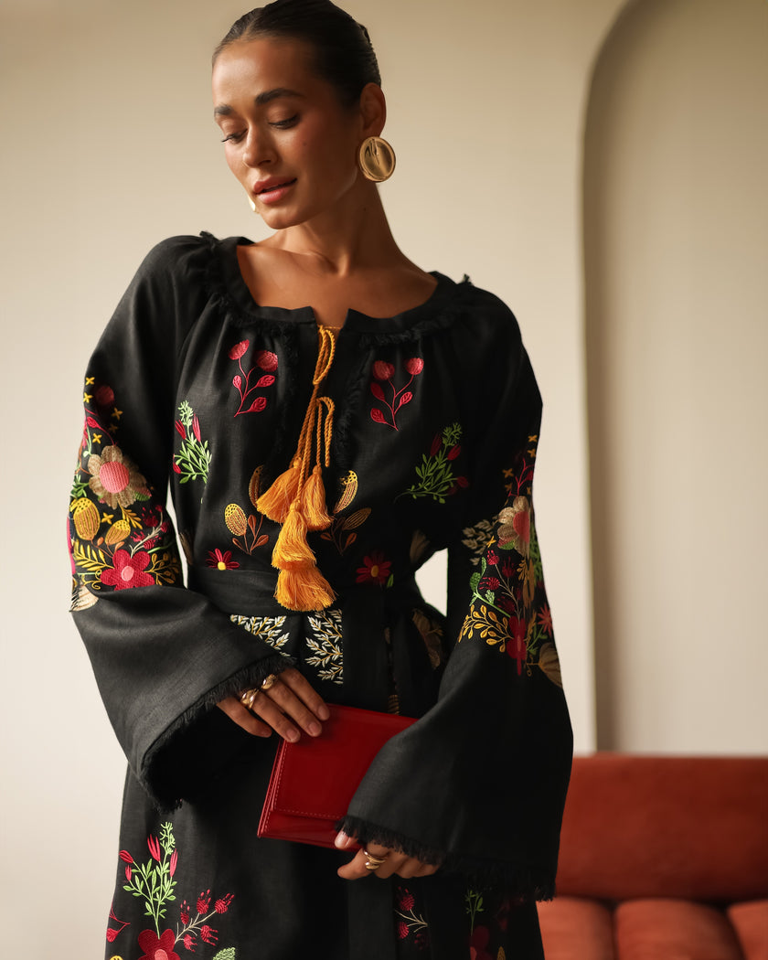 Editorial portrait of model in black floral embroidered linen kaftan maxi dress with mustard tassel ties and red clutch — Zalxndra Resort