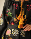 Close-up of mustard yellow corded tassel ties and floral embroidery on black linen kaftan neckline — Zalxndra Resort