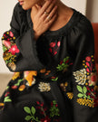 Detail view of floral embroidery and raw-fringed neckline on black linen kaftan dress, styled with gold rings — Zalxndra Resort