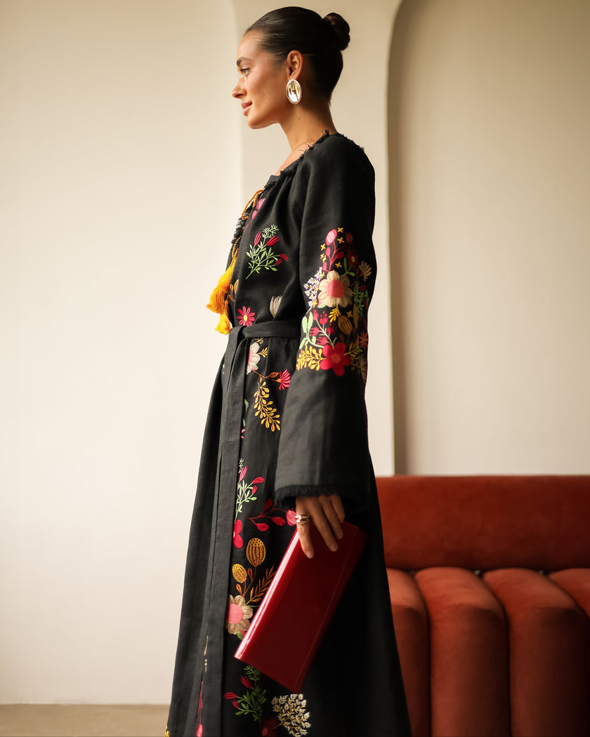 Side profile view of black floral embroidered linen kaftan maxi dress styled with red clutch — Zalxndra Resort