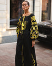 Black linen kaftan maxi dress with gold geometric embroidery, balloon sleeves and gold tassel ties, styled on city street, editorial view - Zalxndra Resort