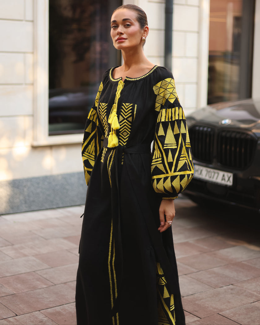Black linen kaftan maxi dress with gold geometric embroidery, balloon sleeves and gold tassel ties, styled on city street, editorial view - Zalxndra Resort