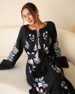 Black linen kaftan maxi dress with pastel floral embroidery and lilac tassel ties styled seated on white sofa - Zalxndra Resort