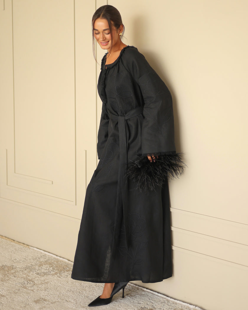 Black linen kaftan maxi dress with tonal floral embroidery, frayed bell sleeves, and tassel ties styled with feather clutch - Zalxndra Resort