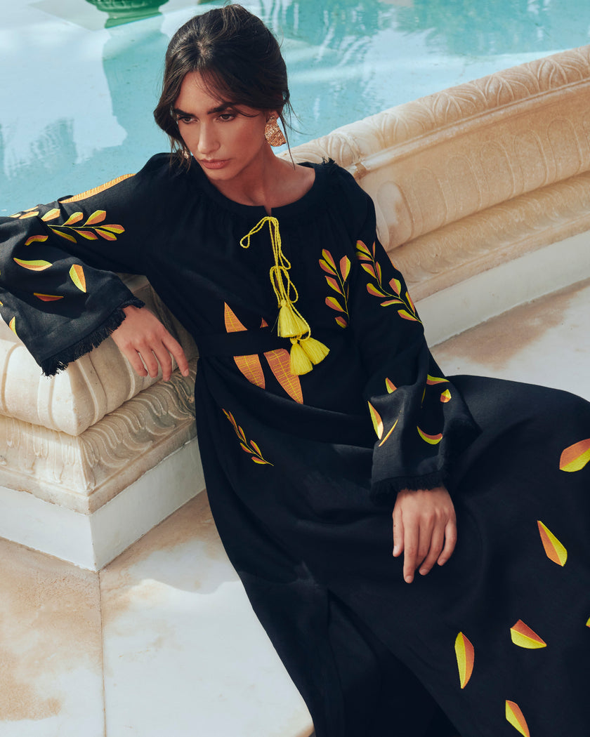 Black linen kaftan maxi dress with yellow and orange leaf embroidery, angel sleeves with frayed trim and yellow tassel ties, styled poolside, editorial view - Zalxndra Resort
