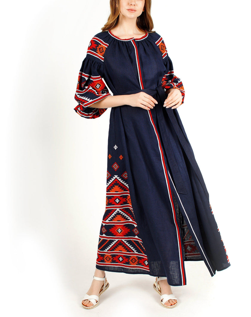 Navy blue linen kaftan maxi dress with red, orange, and white hand-embroidered cross-stitch geometric pattern, balloon sleeves, and self-tie belt on model, full-length view - Zalxndra Resort