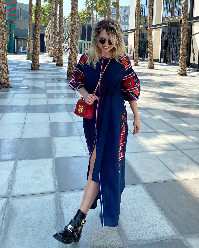 Navy blue linen kaftan maxi dress with red and orange hand-embroidered cross-stitch, balloon sleeves, self-tie belt, and front slit, full-length lifestyle view - Zalxndra Resort