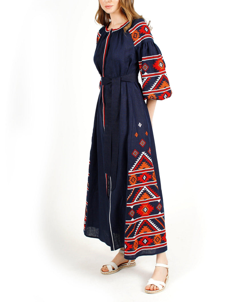 Navy blue linen kaftan maxi dress with red, orange, and white hand-embroidered cross-stitch, balloon sleeves, and self-tie belt, side view - Zalxndra Resort