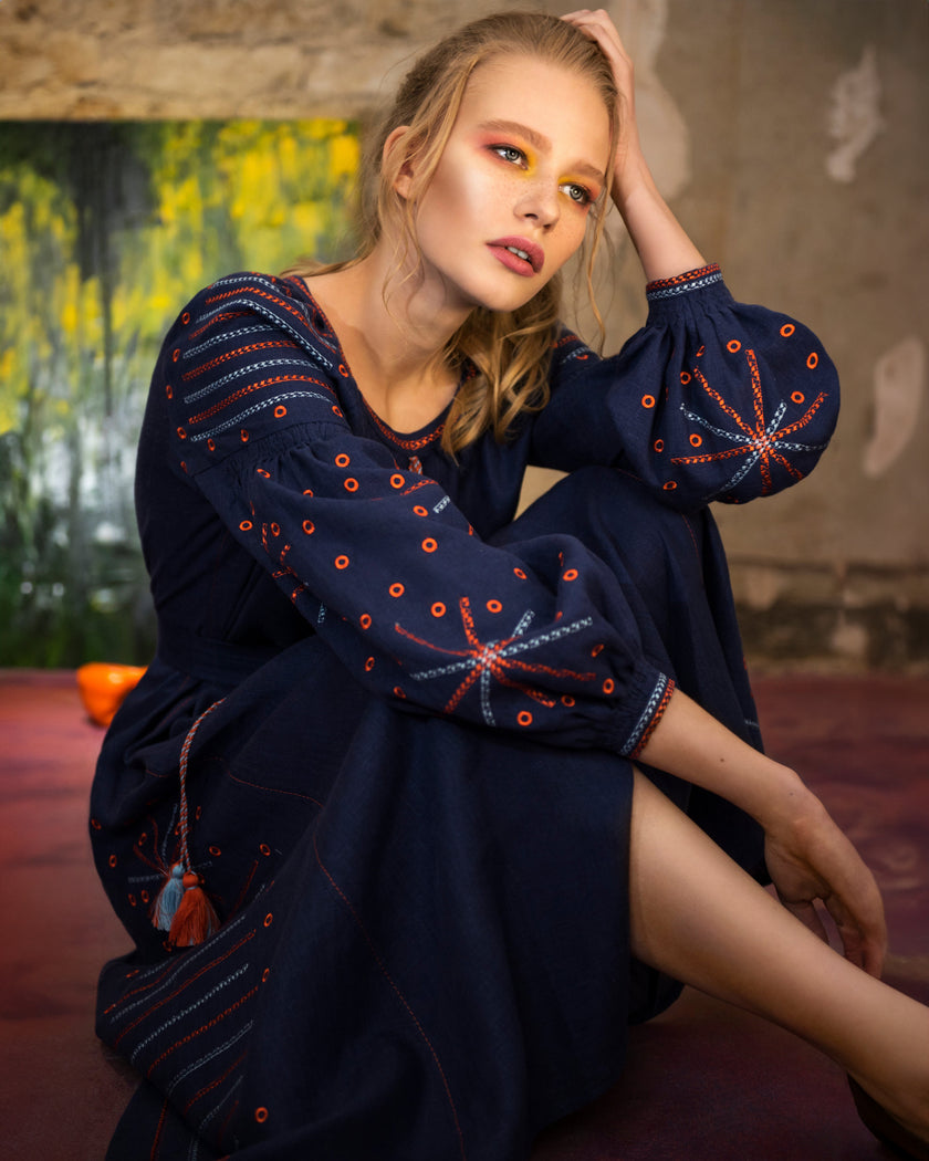 Seated model in navy linen kaftan maxi dress with orange and blue geometric embroidery and tassel ties - Zalxndra Resort