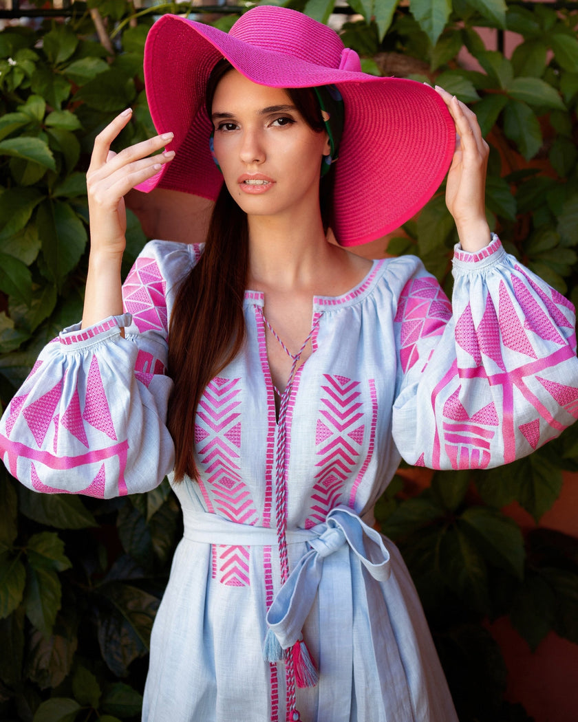 Powder blue linen kaftan maxi dress with pink geometric embroidery, balloon sleeves and self-tie belt, styled with pink wide-brim hat, portrait view - Zalxndra Resort
