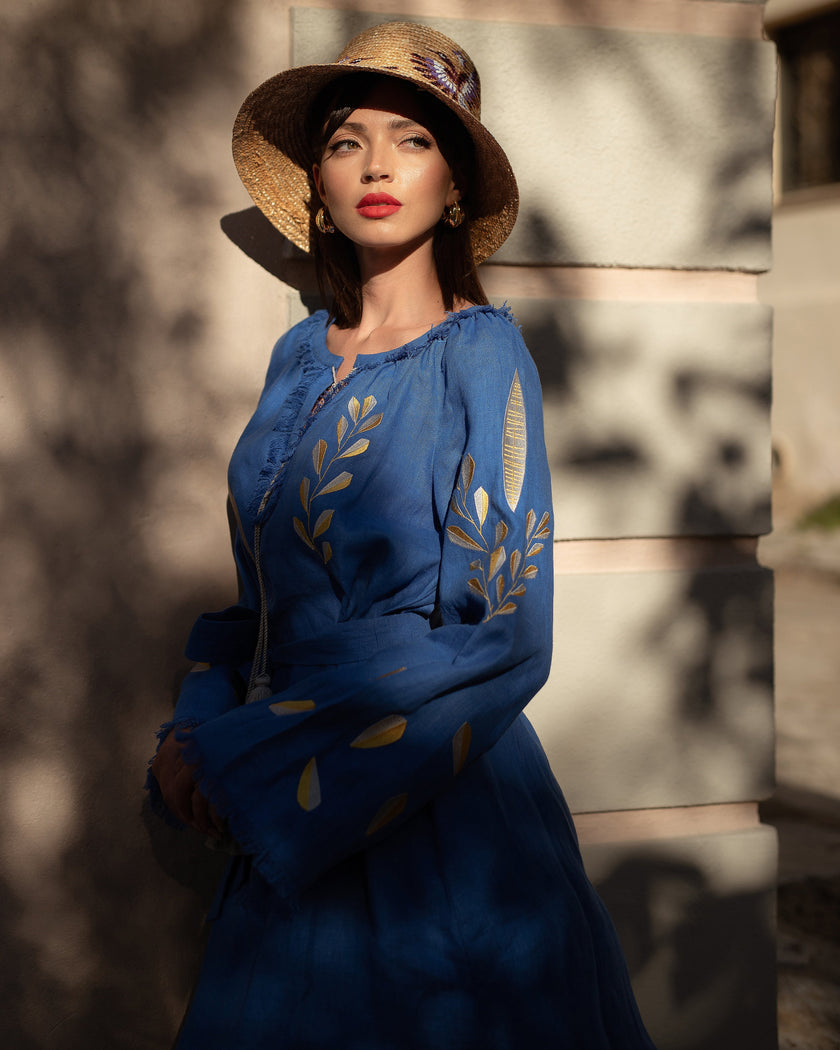 Royal blue linen kaftan maxi dress with gold leaf embroidery, angel sleeves with frayed trim, styled with straw hat, editorial portrait view - Zalxndra Resort