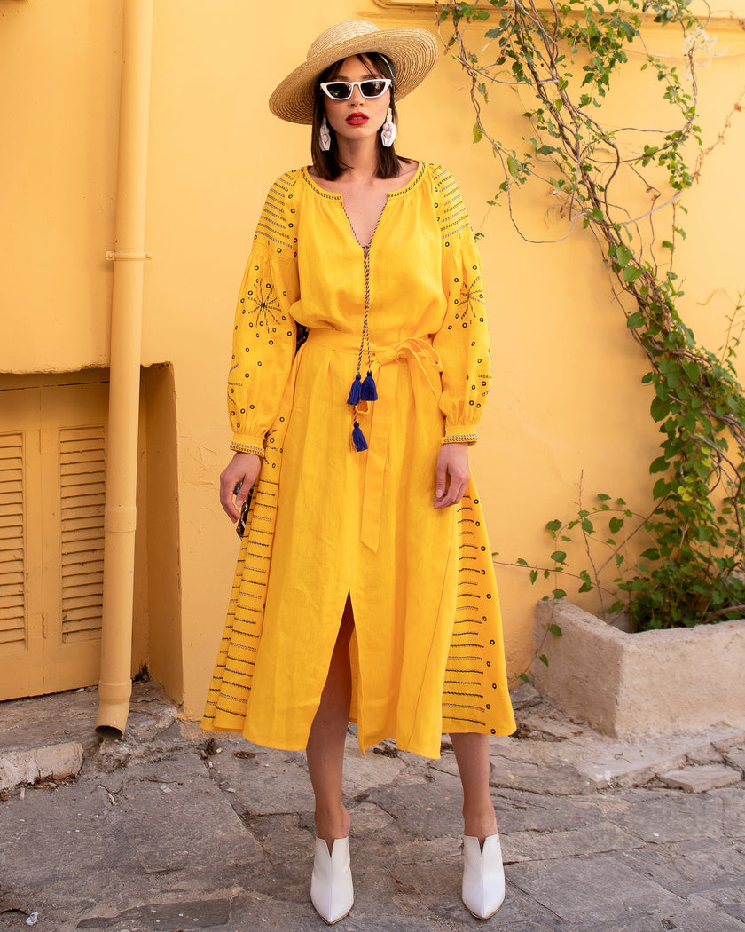 Saffron yellow linen kaftan maxi dress with navy geometric embroidery, balloon sleeves and tassel tie belt, styled with straw hat and white boots, lifestyle view - Zalxndra Resort