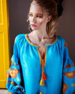 Portrait of model in turquoise linen kaftan midi dress with orange and yellow geometric embroidery and tassel ties - Zalxndra Resort