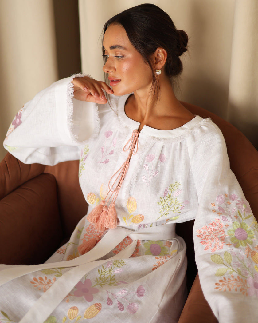Bell sleeve with raw-fringed cuff and pastel embroidery on white linen kaftan, shown on seated model — Zalxndra Resort