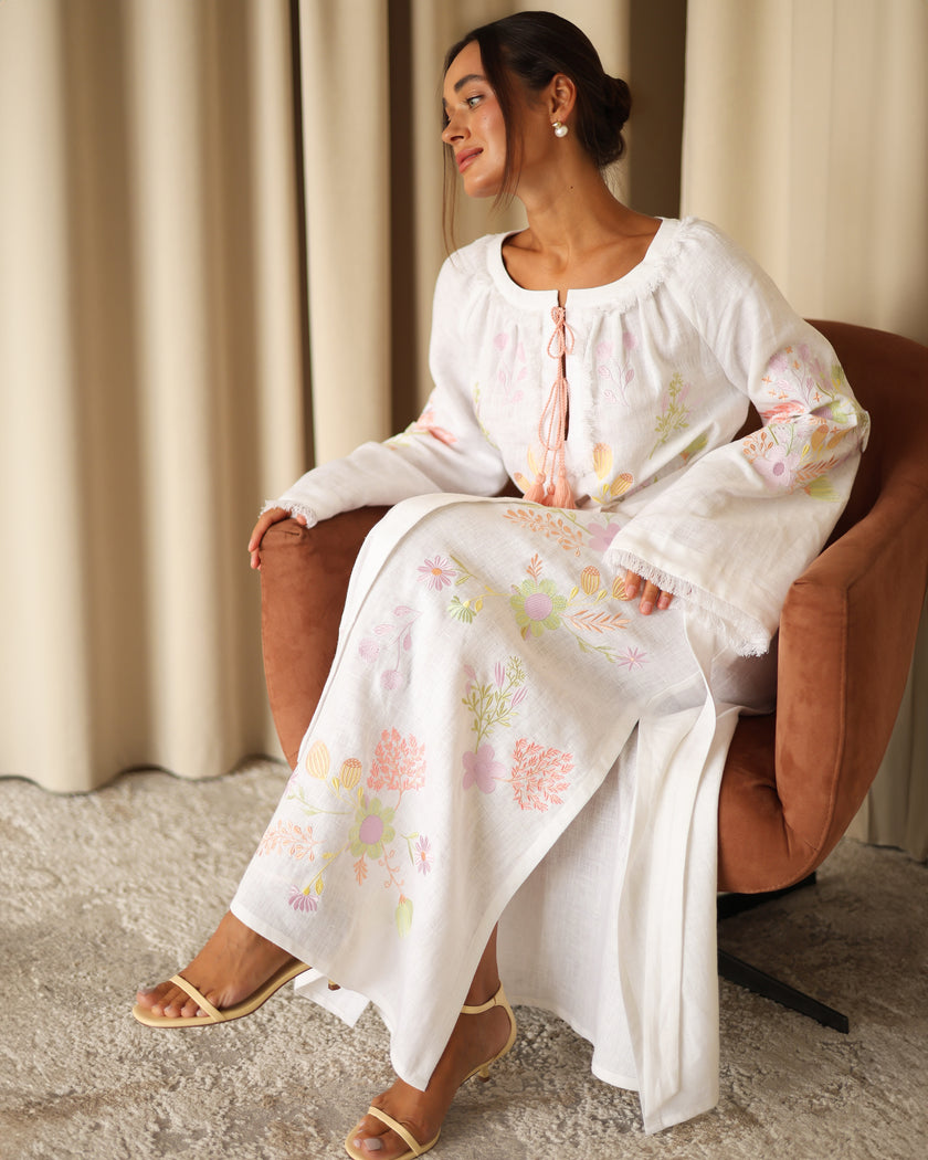 Model seated in white pastel floral embroidered linen kaftan maxi dress styled with leather sandals — Zalxndra Resort