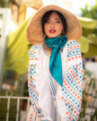 White linen maxi dress with teal and orange geometric embroidery and balloon sleeves, styled with straw hat and teal silk scarf, portrait view - Zalxndra Resort