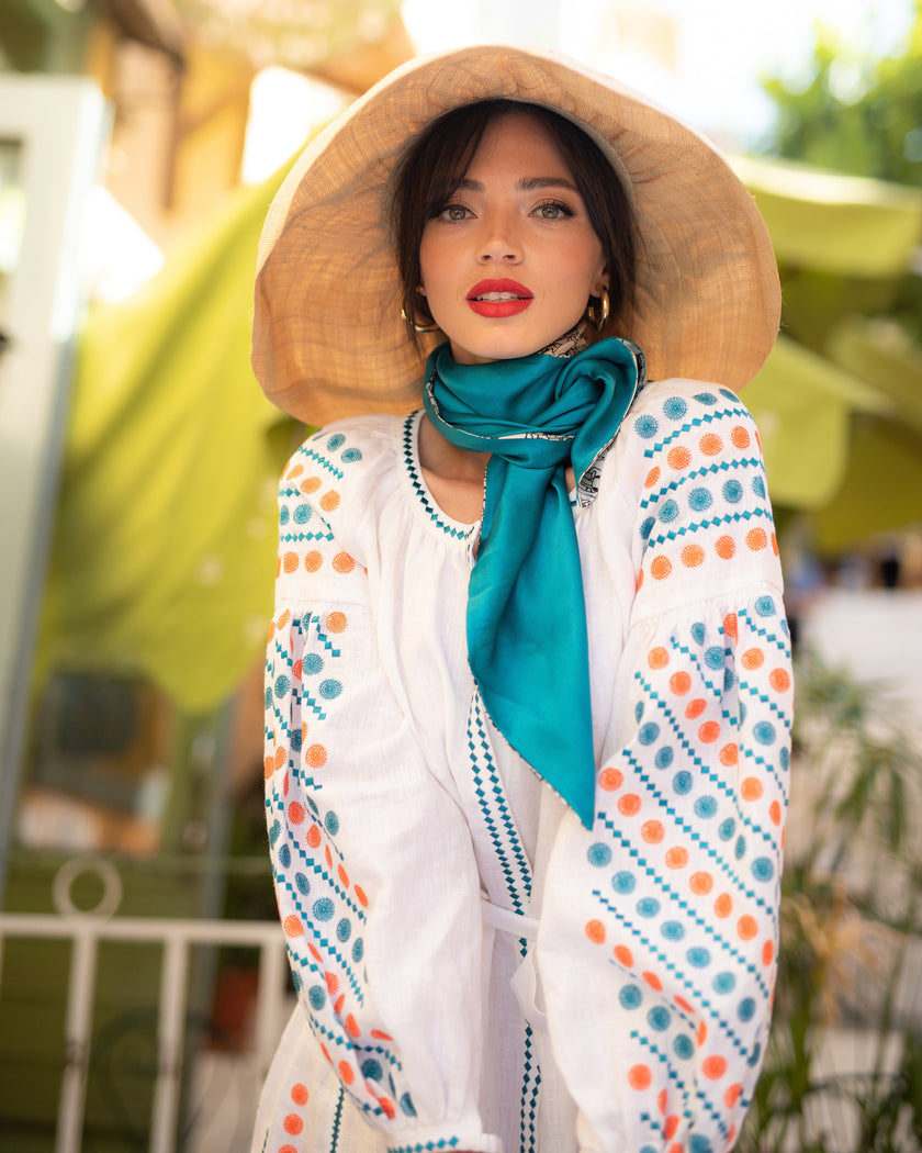 White linen maxi dress with teal and orange geometric embroidery and balloon sleeves, styled with straw hat and teal silk scarf, portrait view - Zalxndra Resort