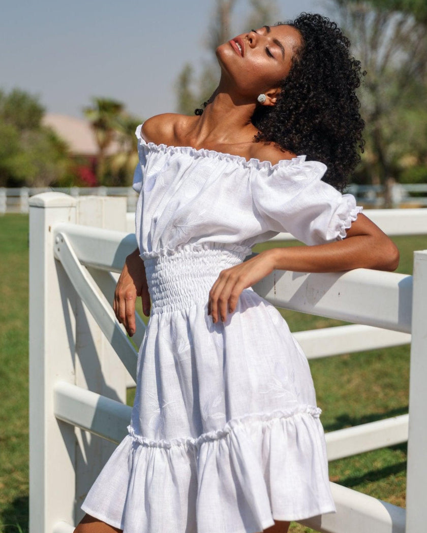 Editorial view of white linen off-shoulder mini dress with tonal lemon embroidery, puff sleeves, and ruffle hem - Zalxndra Resort