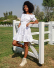 White linen off-shoulder mini dress with tonal lemon embroidery, puff sleeves, and ruffle hem styled in outdoor setting - Zalxndra Resort