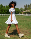 Side view of white linen off-shoulder mini dress with tonal lemon embroidery, puff sleeves, and ruffle hem - Zalxndra Resort