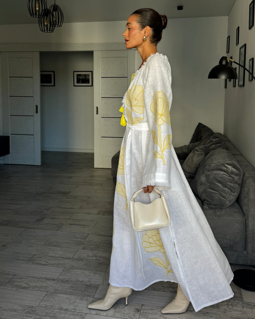 Side profile of white linen kaftan maxi dress with yellow outlined floral embroidery and angel sleeves styled with handbag - Zalxndra Resort
